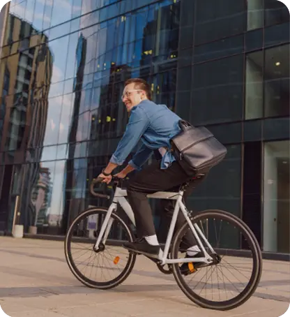 An adult wearing glasses, a blue shirt, black pants, and a black backpack is riding a white bicycle on a city street with tall glass buildings in the background.

Description generated by AI