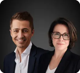 Two adults dressed in business attire are standing close together against a dark background, both smiling gently.

Description generated by AI